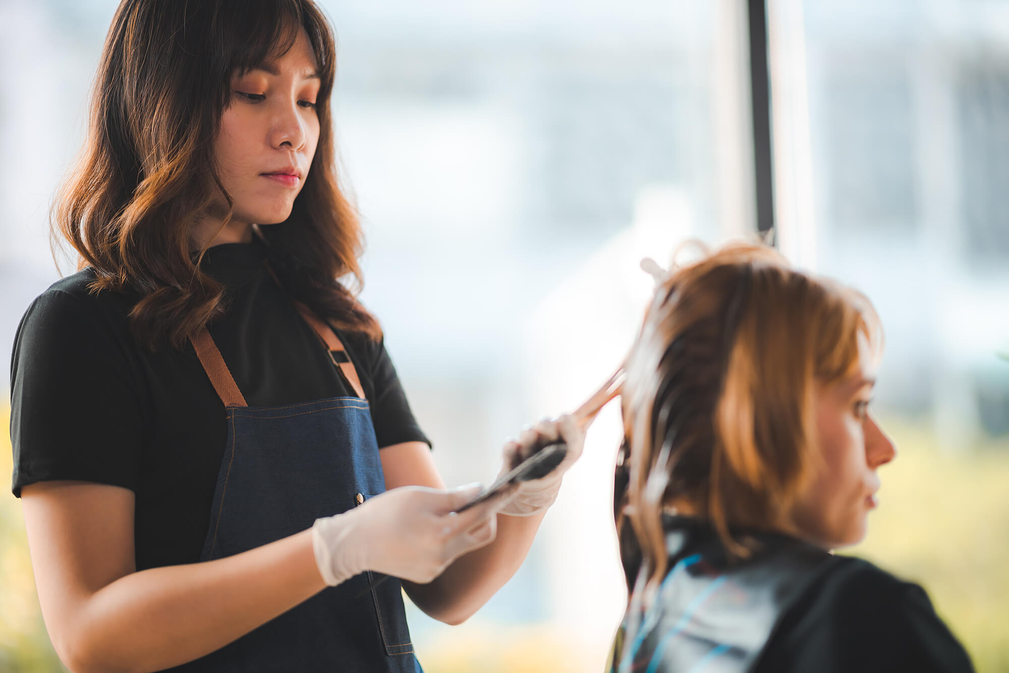 A hairstylist trims or styles a seated client’s hair in a bright, modern salon.